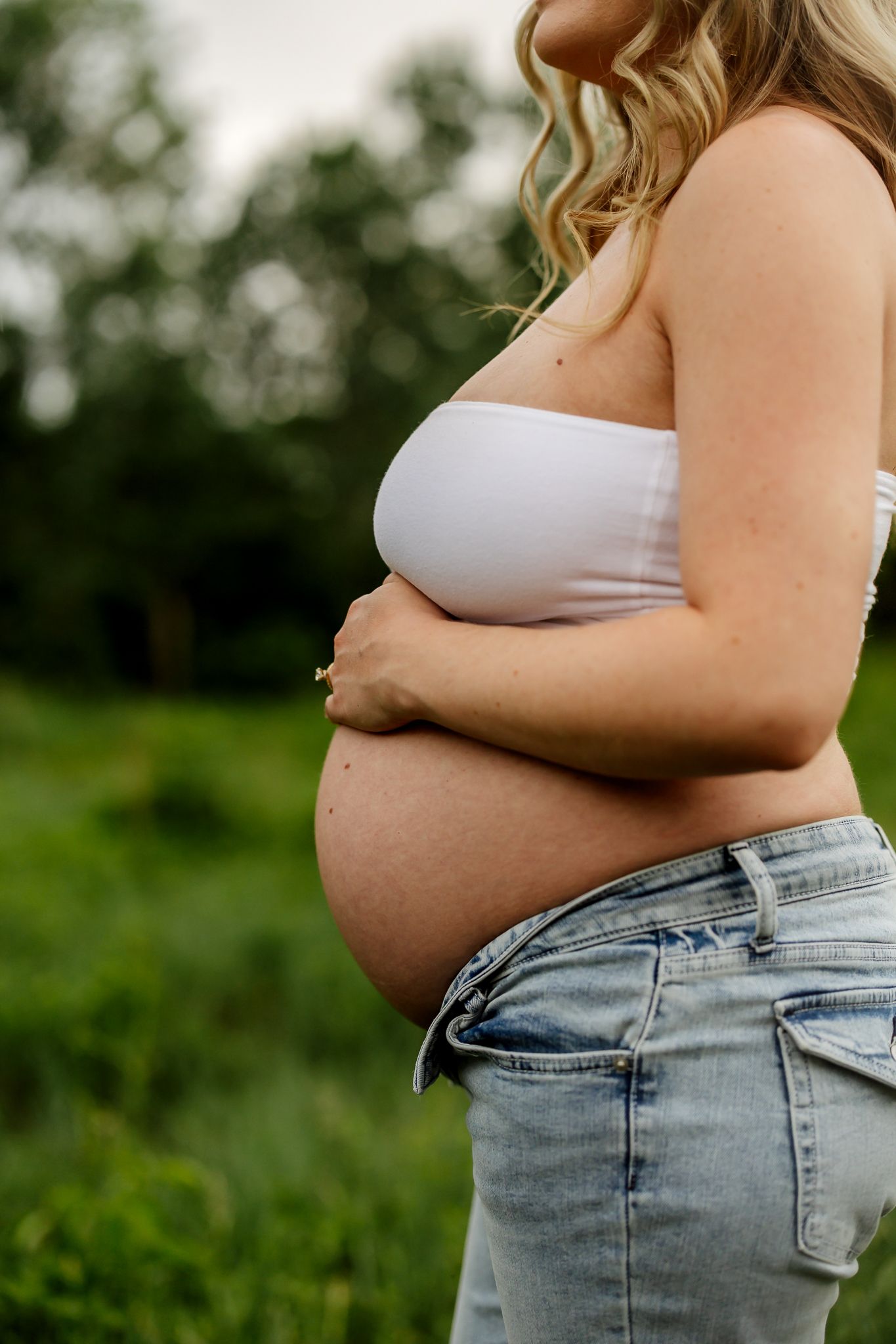 Close-up side profile maternity photo of pregnant woman in white top holding baby bump outdoors.
