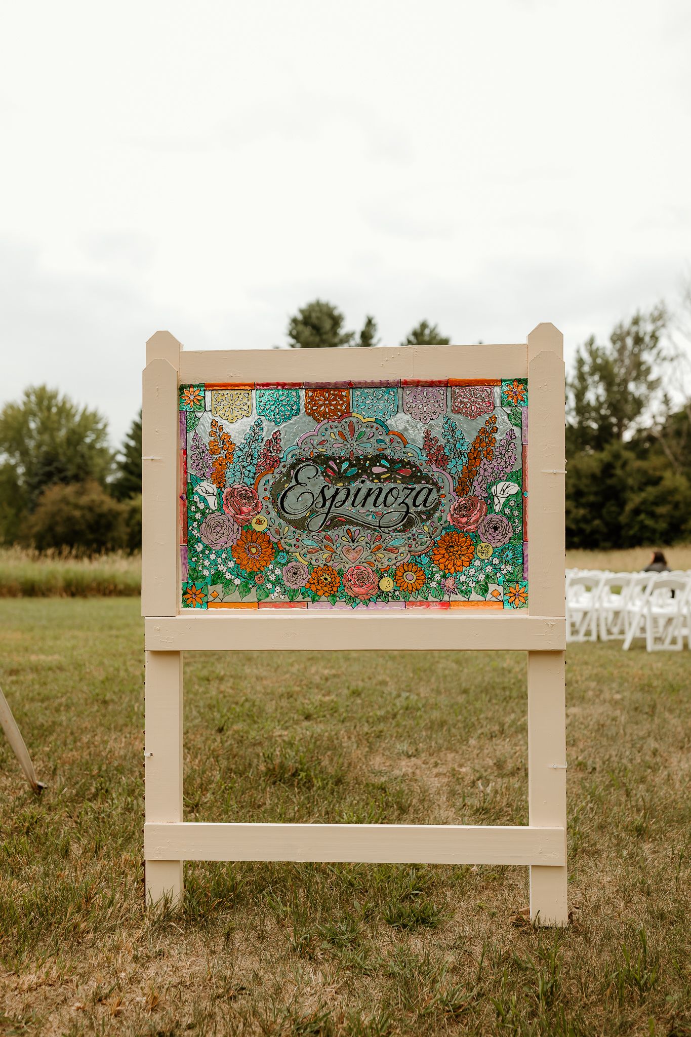 Colorful floral wedding welcome sign for the Espinoza family displayed on a wooden easel at an outdoor ceremony.