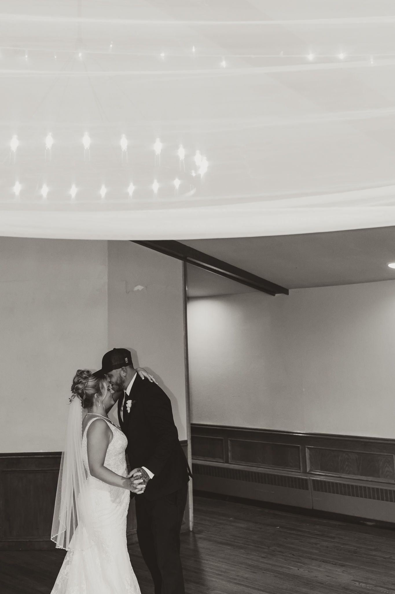 Black and white photo of a bride and groom sharing their first dance kiss at their wedding reception.