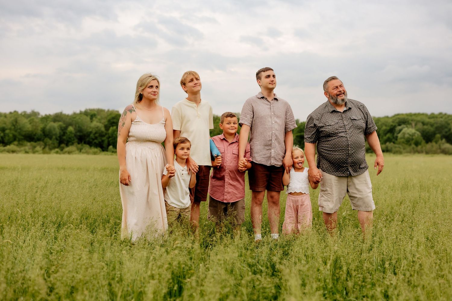 Family of seven standing together in a wide open green field under a cloudy sky.