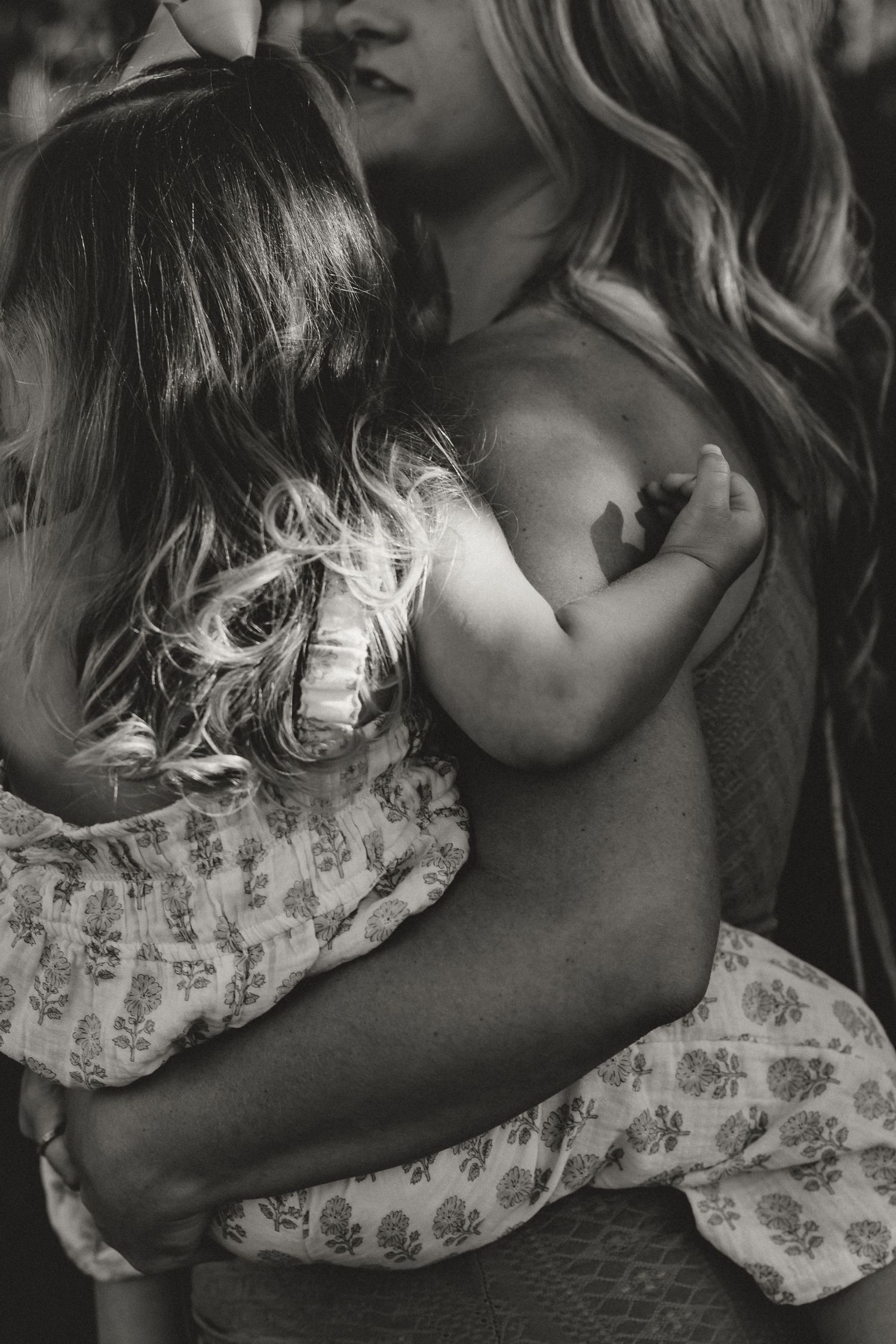 Black and white close-up of a mother tenderly holding a young child in a floral dress.