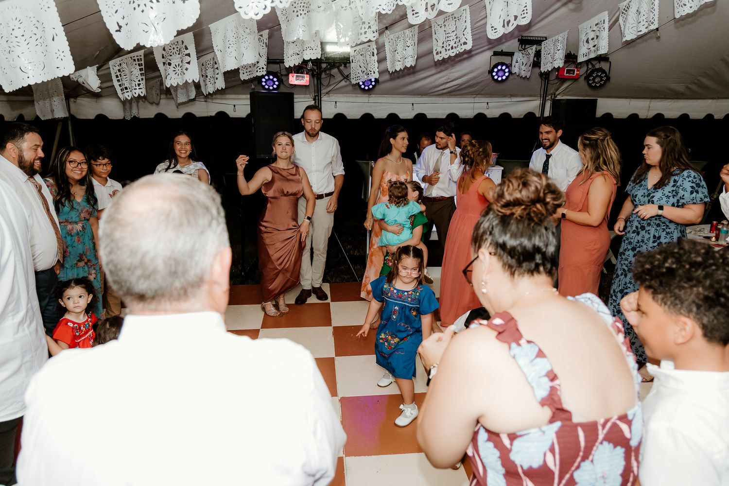 Guests dancing and celebrating at a festive wedding reception under a decorated tent with papel picado banners.