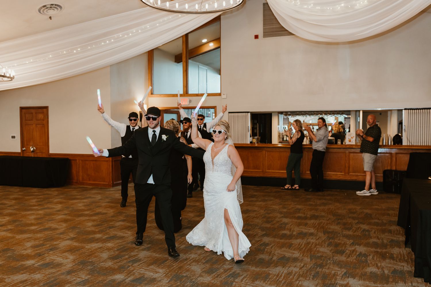 Bride and groom make grand entrance at wedding reception, waving sparklers in elegant ballroom venue.