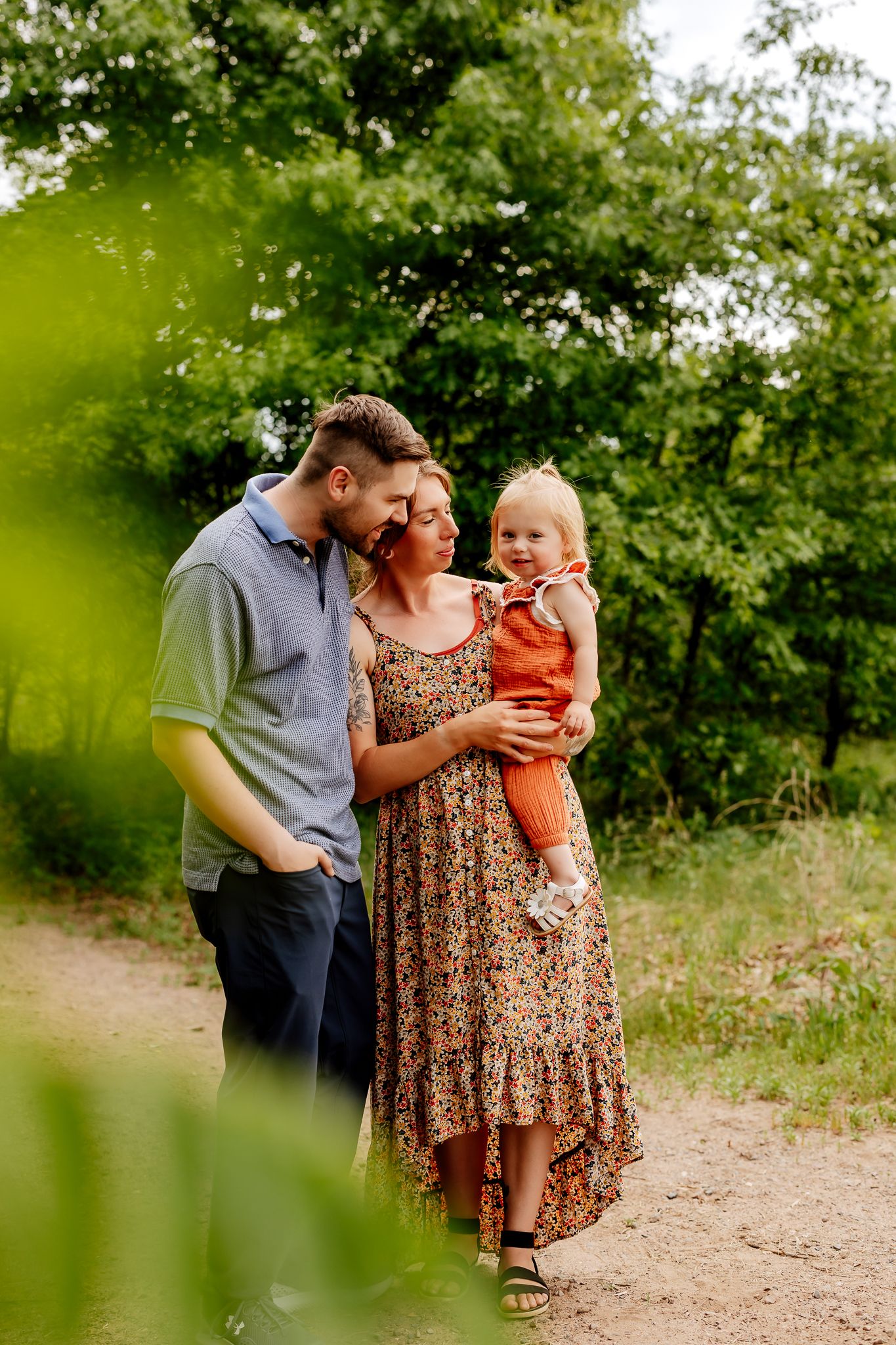 Young couple with their toddler daughter walking on a shaded garden path.