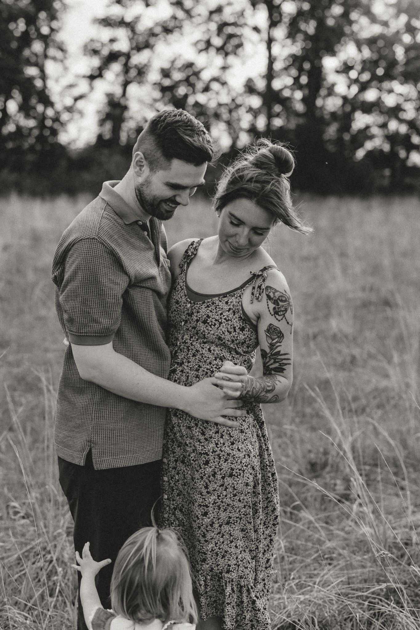 Black and white photo of a couple tenderly cradling a pregnant belly in an open grassy field.