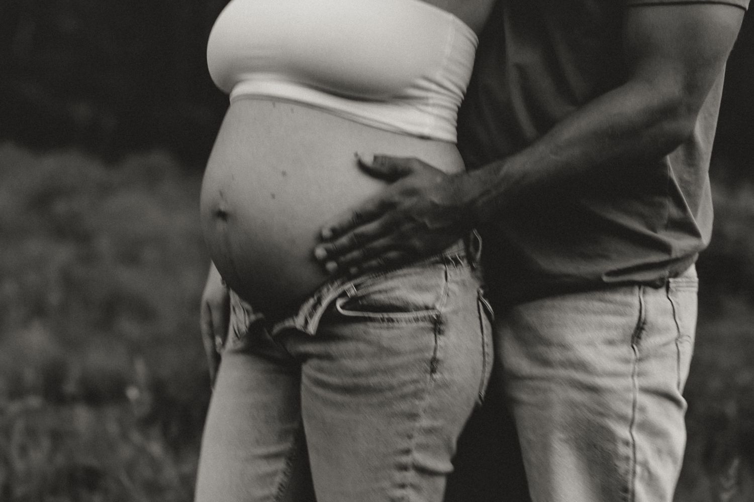 Black and white close-up of pregnant woman with partner's hand gently resting on her baby bump.
