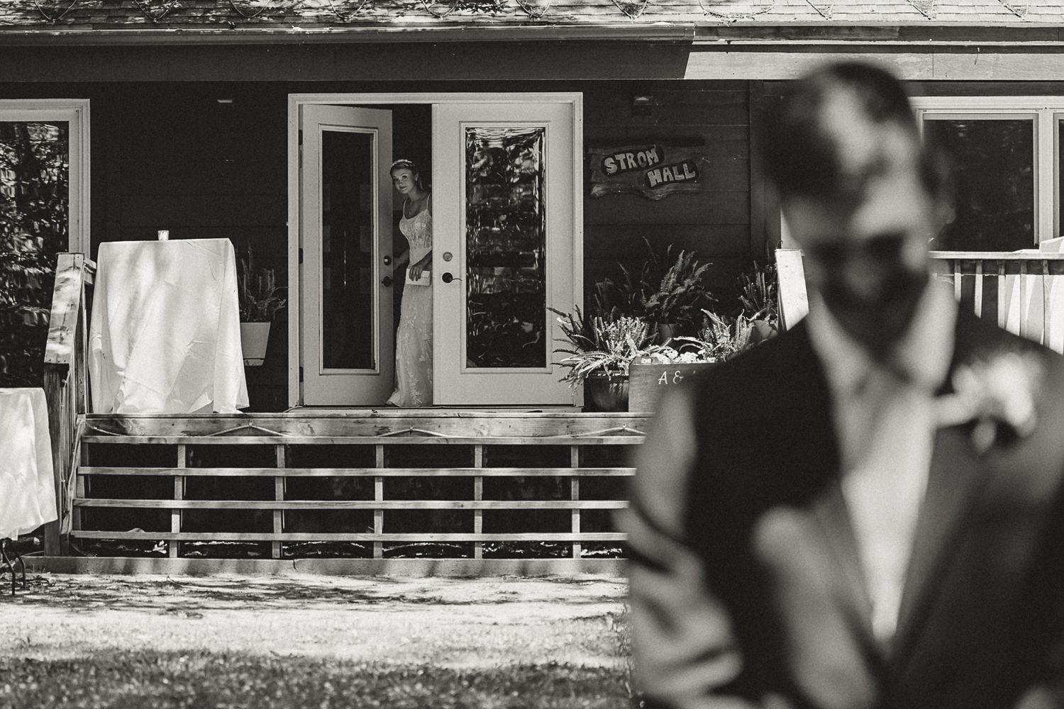 Black and white wedding photo of bride emerging from cabin doorway while groom stands in foreground.