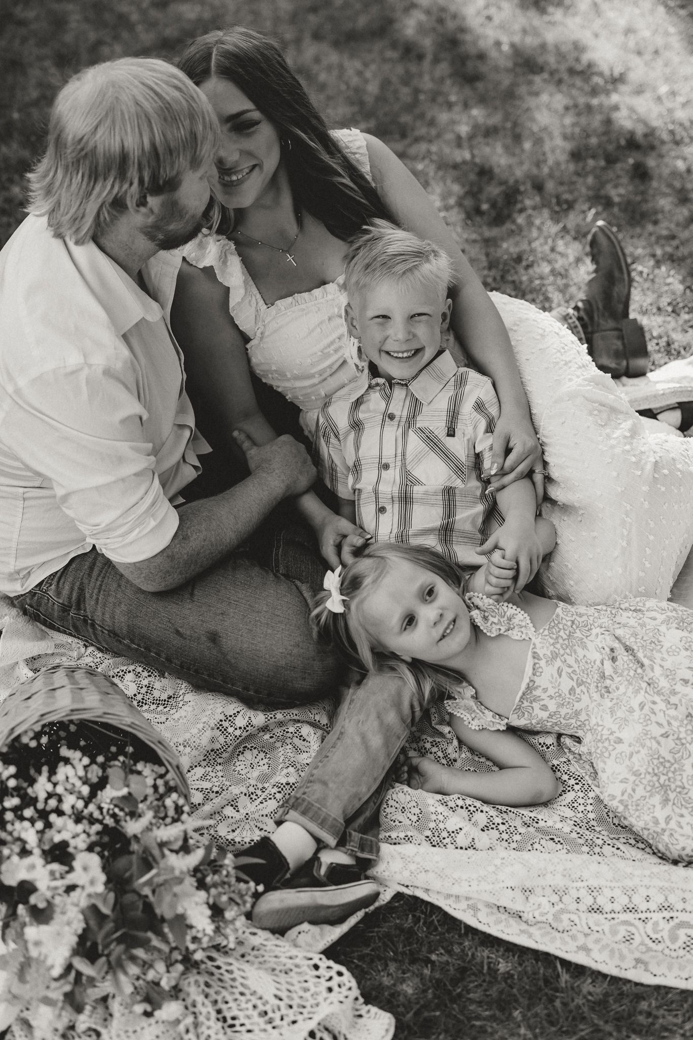 Black and white photo of a loving family of four relaxing on a blanket outdoors during a picnic session.