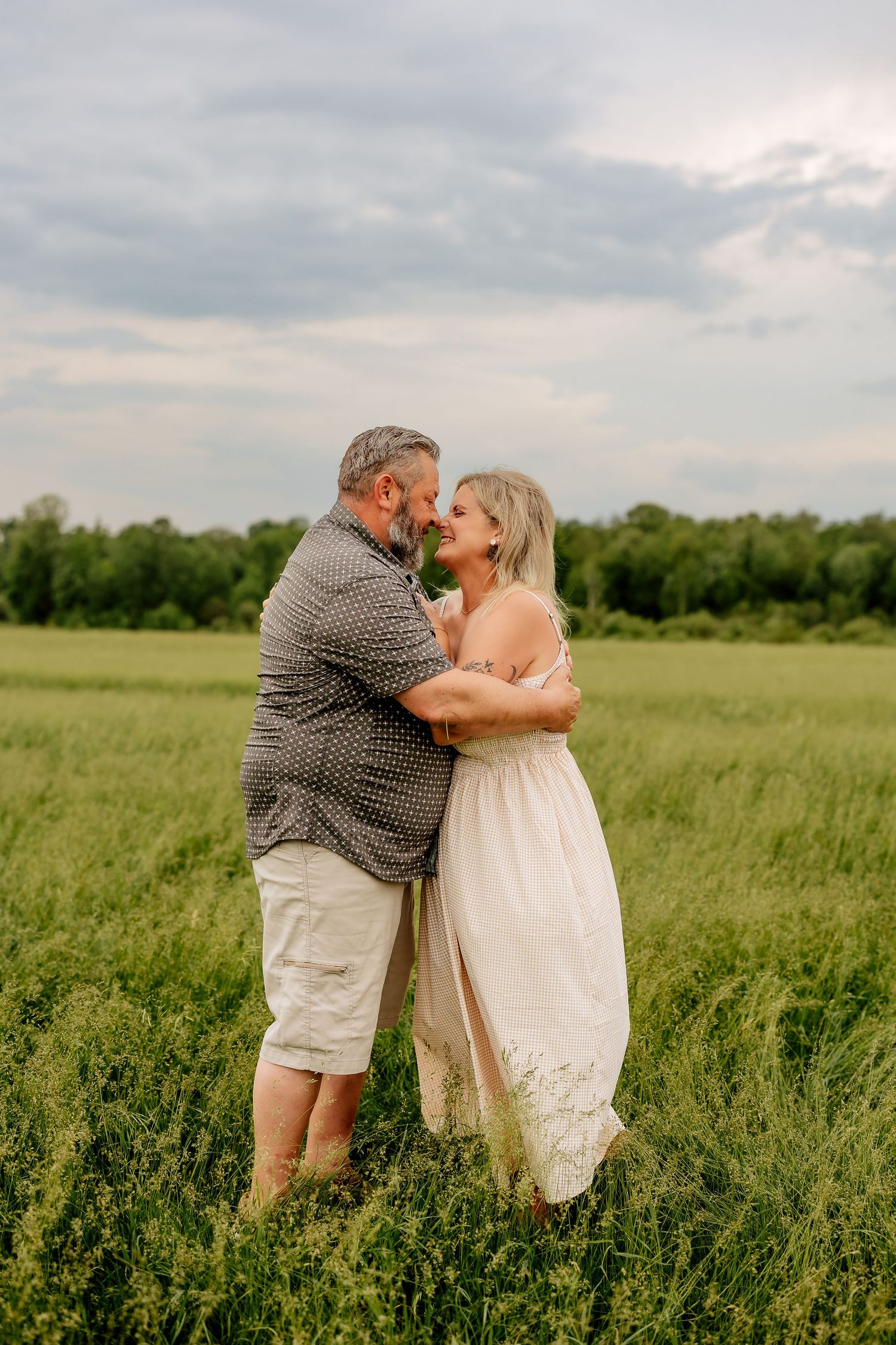 Couple gazing lovingly at each other while embracing in a green summer field.