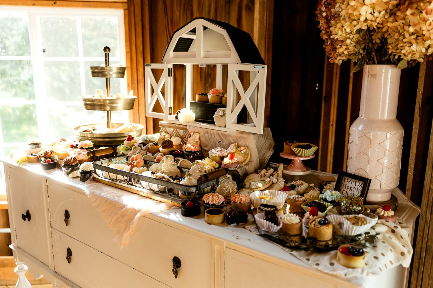 Rustic barn-themed dessert table with white dresser, tiered stands, and assorted sweets at a country wedding reception.