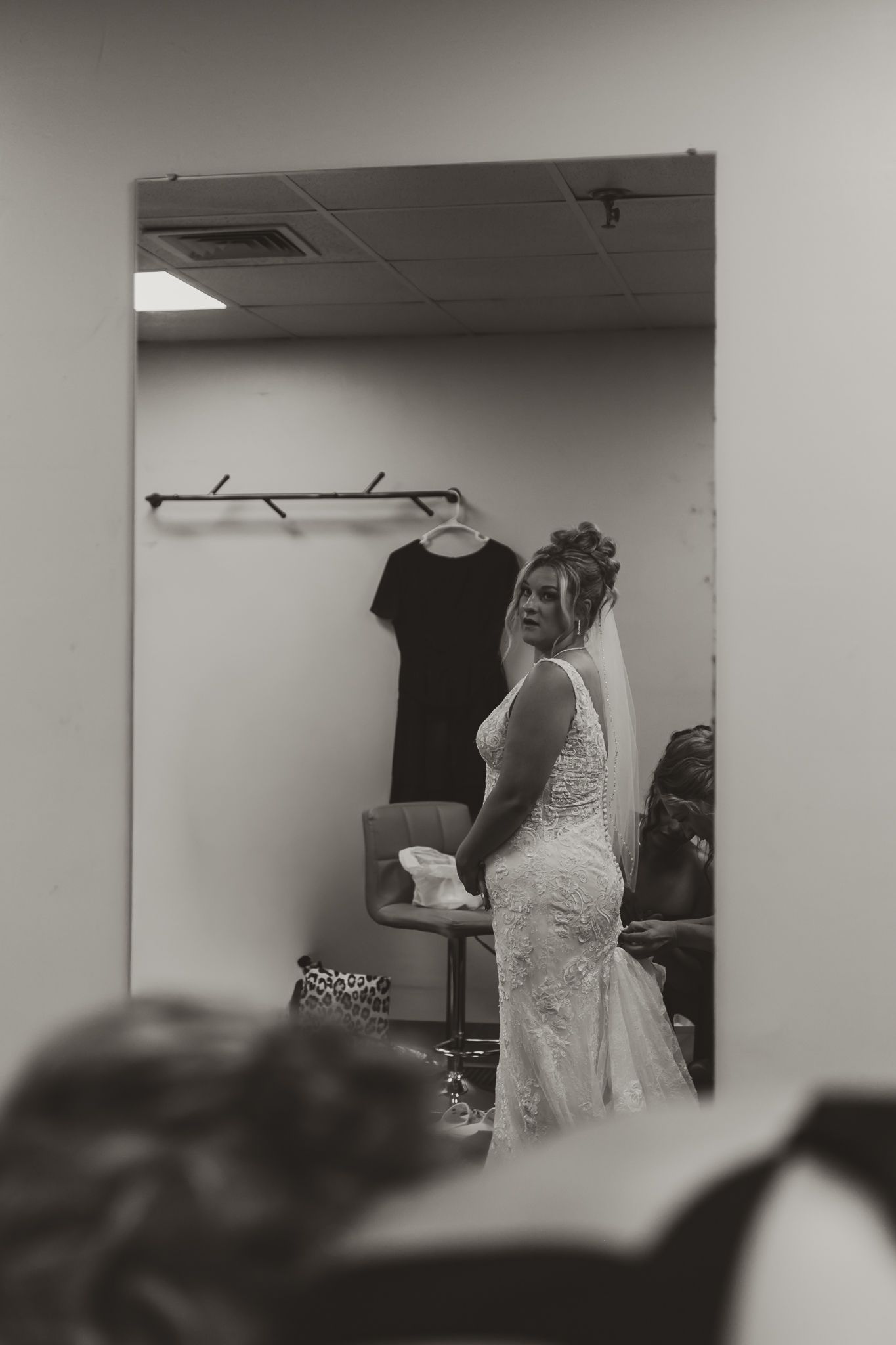 Bride in lace wedding dress and veil reflected in mirror, black and white photo in bridal suite.