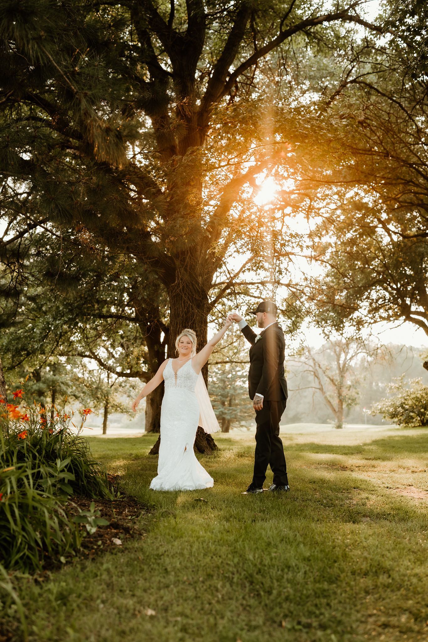Bride and groom holding hands under a sunlit tree in a lush garden during golden hour wedding portraits.