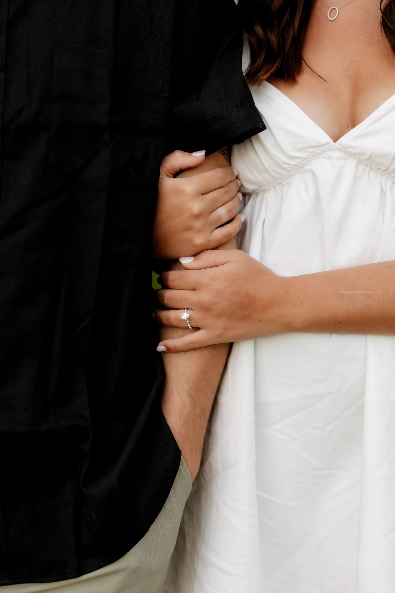 Close-up of an engaged couple embracing, woman wearing a diamond ring in a white dress.