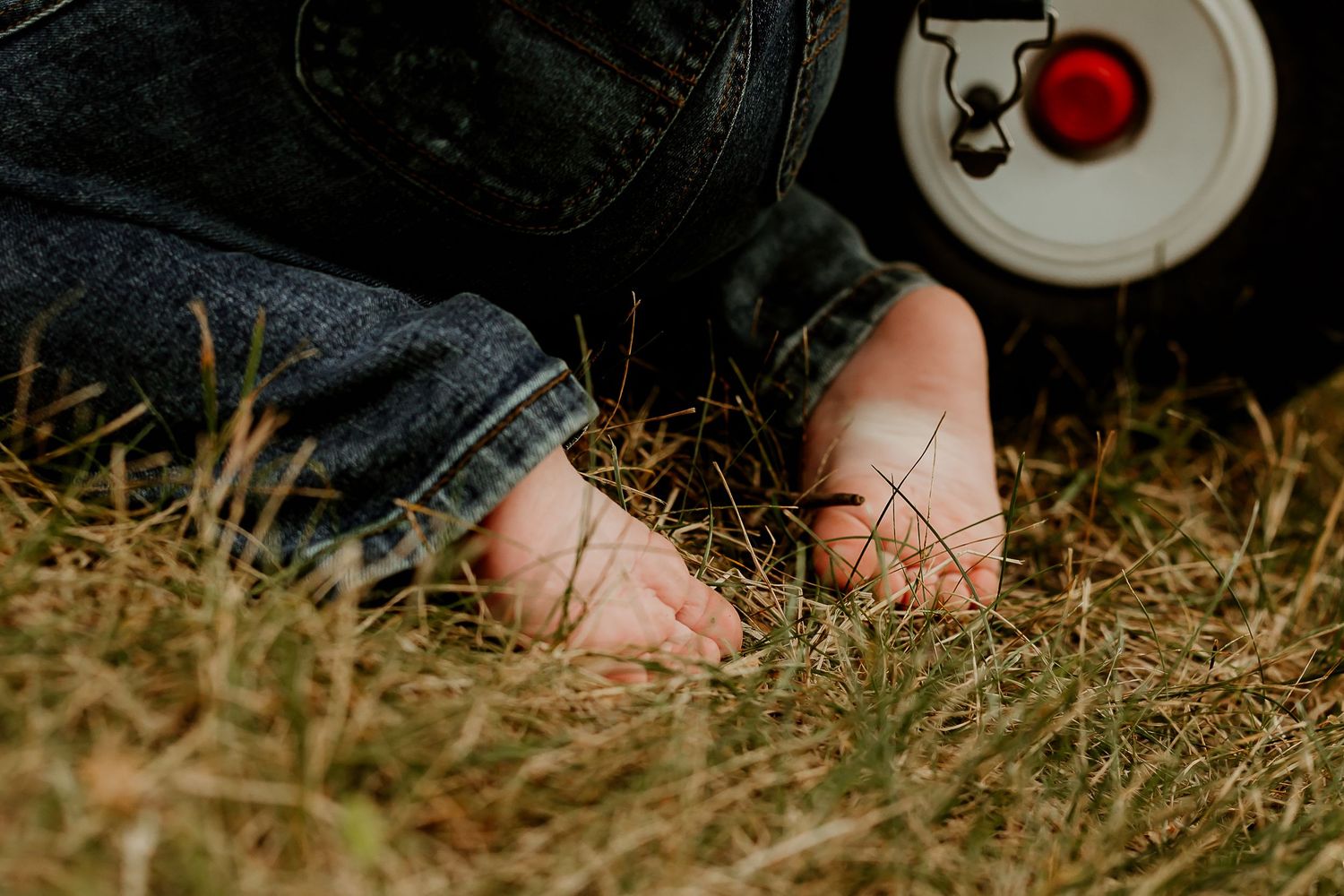 Bare feet of a child resting on dry grass beside a white toy wheel outdoors.