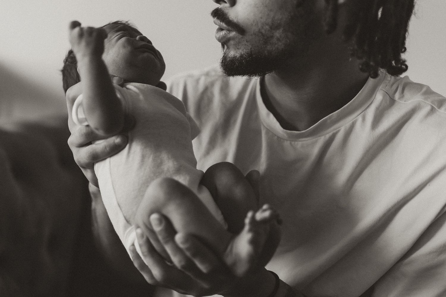Black and white photo of a father tenderly holding his newborn baby, showcasing a precious bonding moment.