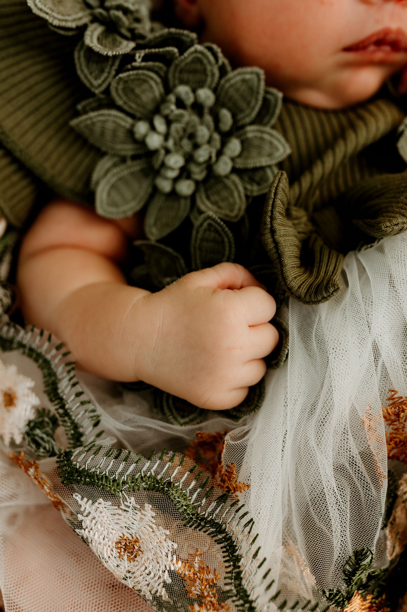 Close-up of a sleeping baby's hand resting on a floral embroidered dress with green knit flower details.
