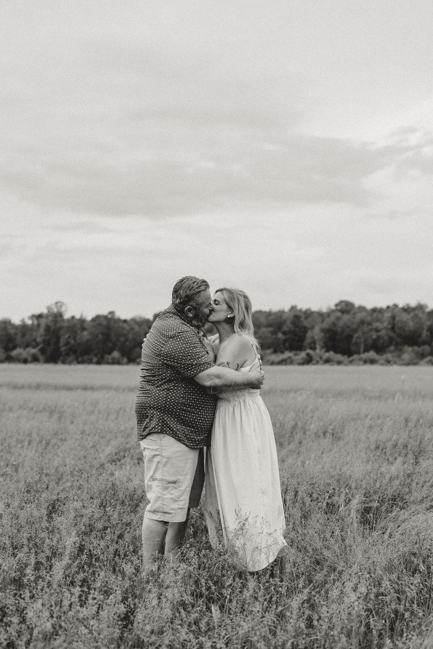 Black and white photo of a couple kissing in an open grassy field.