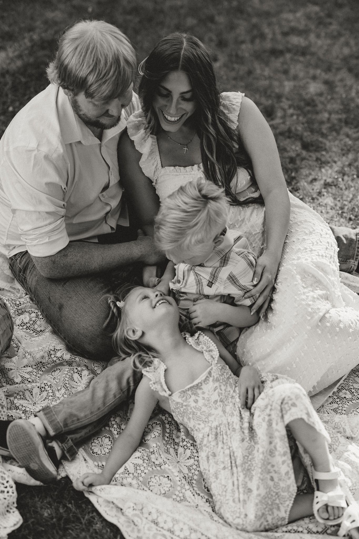 Black and white photo of a happy family of four sitting on a blanket outdoors, laughing together.