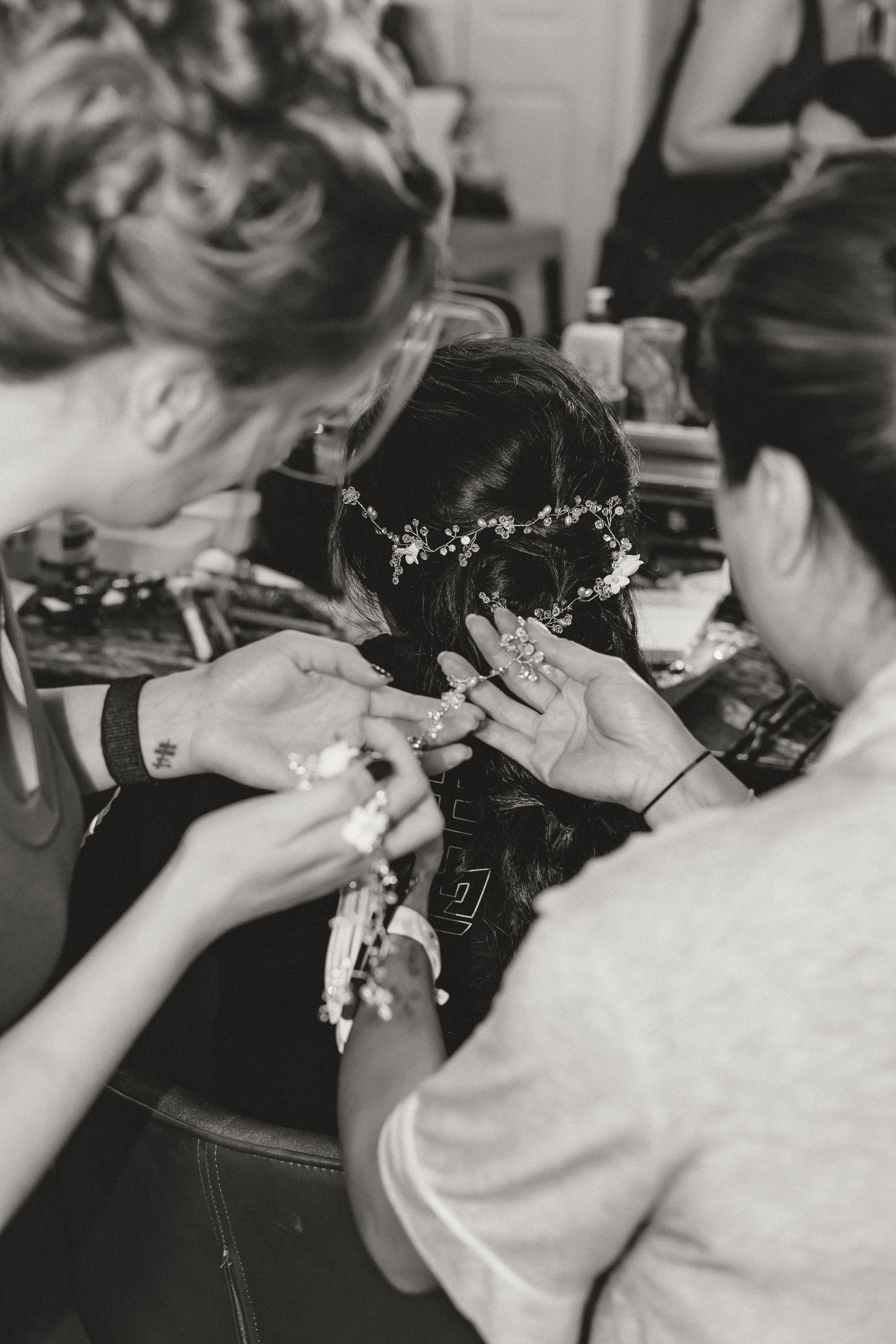 Two stylists arranging a floral hair crown on a bride's dark updo hairstyle in black and white photo.