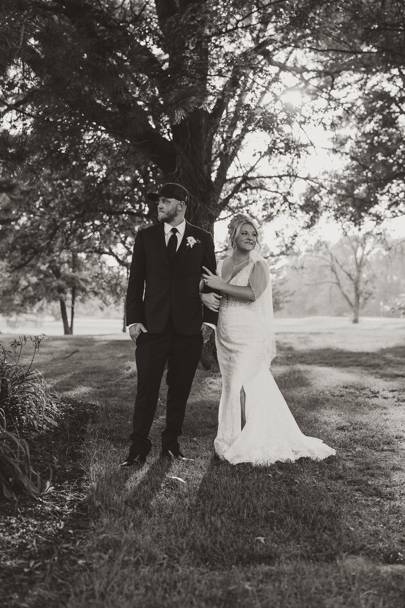 Black and white photo of a bride and groom standing under a large tree on their wedding day.