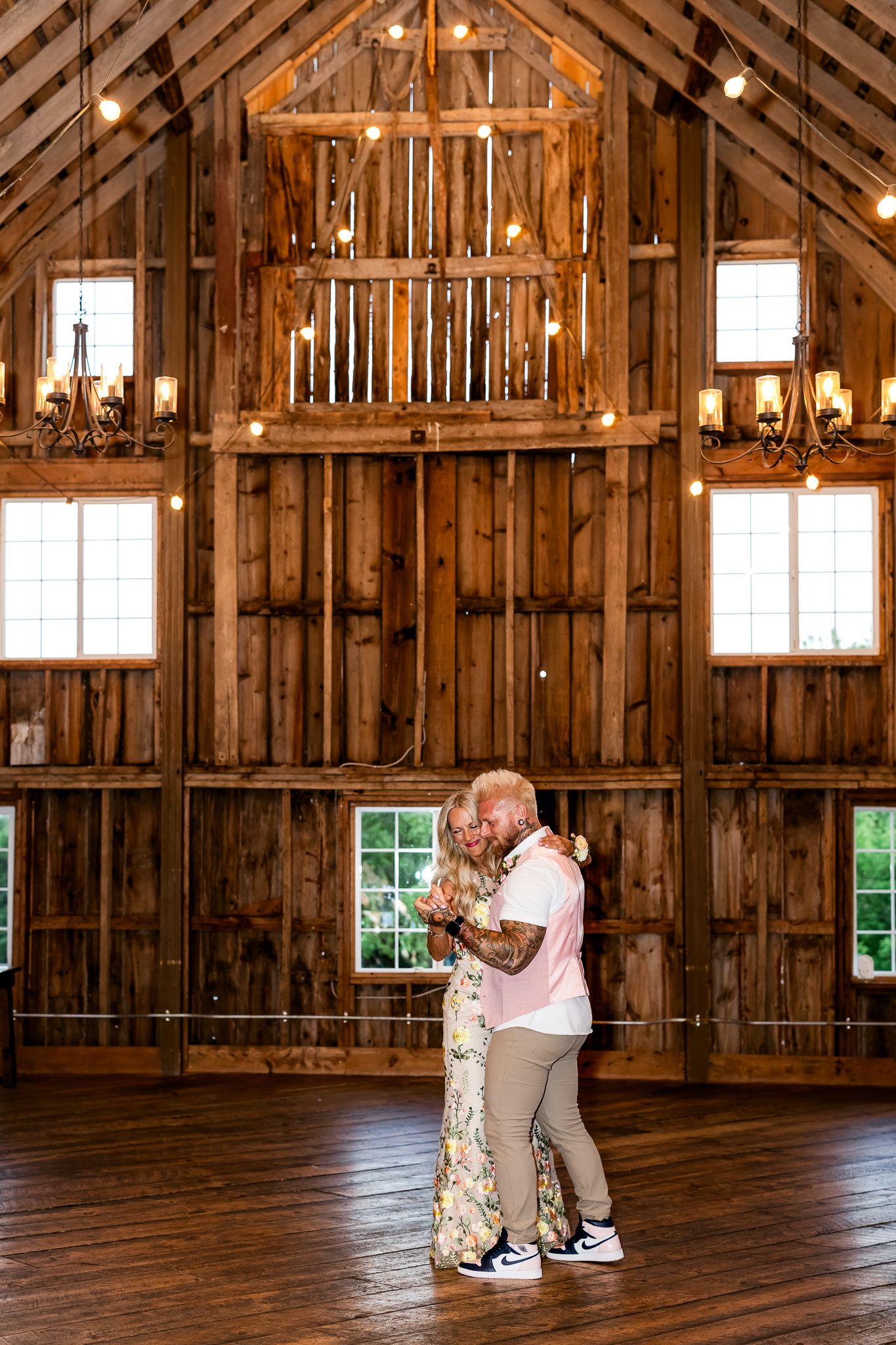 Couple sharing a romantic dance in a rustic wooden barn venue with chandeliers and string lights overhead.