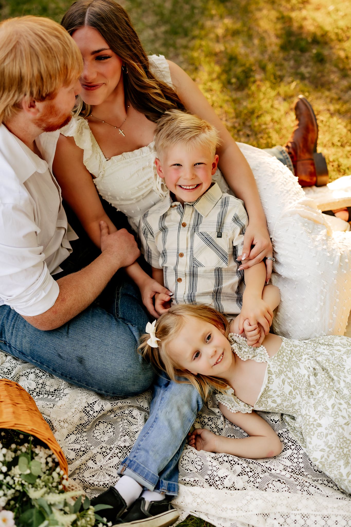A joyful family of four shares a warm moment together on a lace blanket during an outdoor picnic photo session.