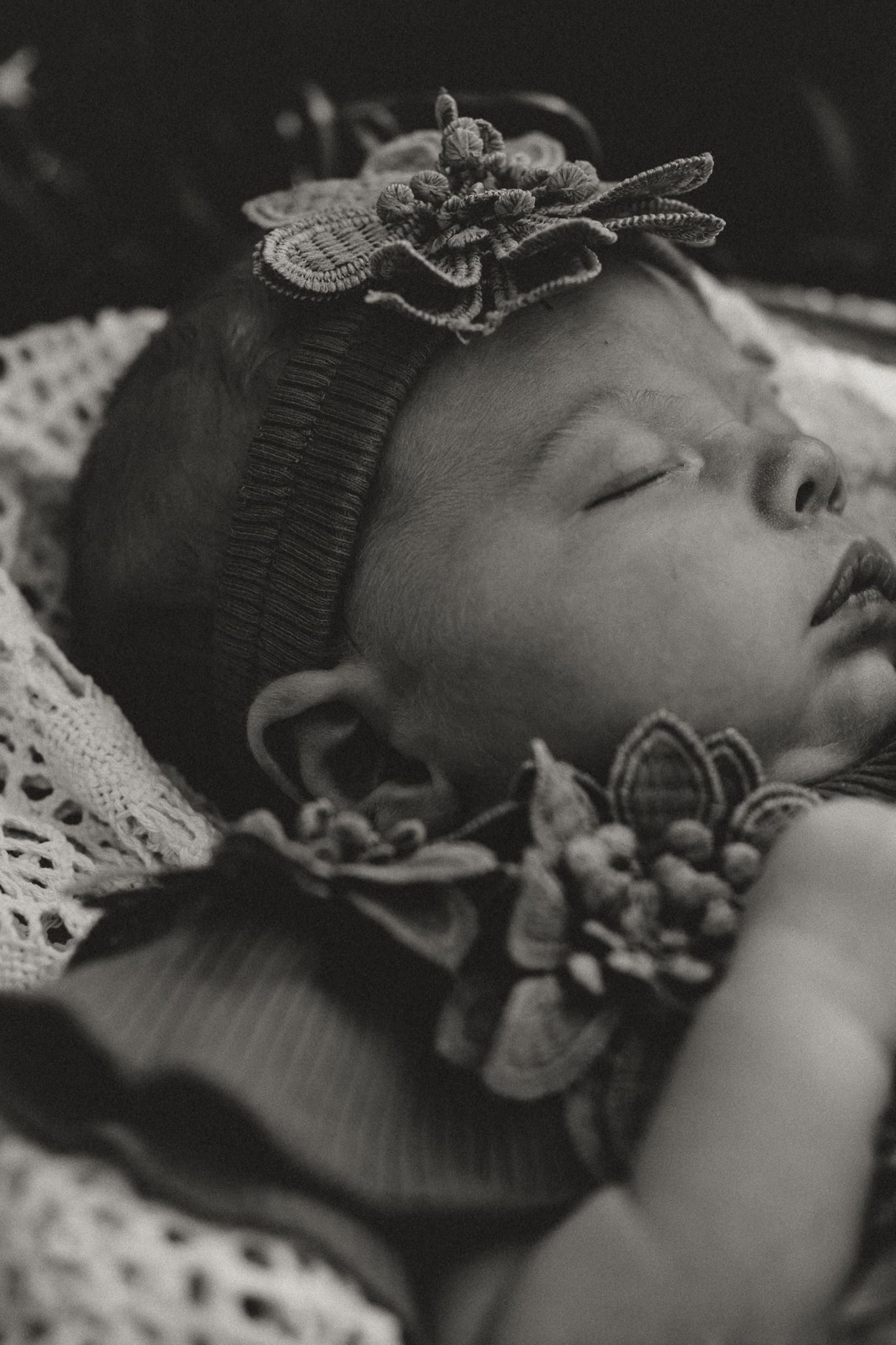 Black and white photo of a sleeping newborn baby wearing a knit hat with a floral decoration.