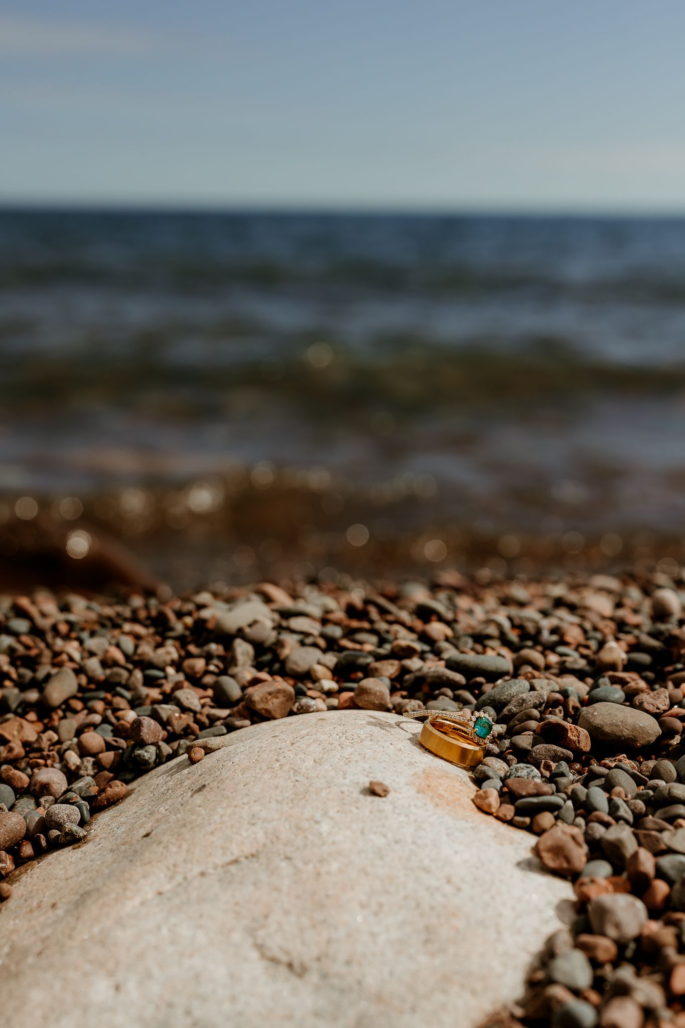 Close-up of colorful pebbles and a large rock on a rocky beach shoreline with ocean waves in the background.