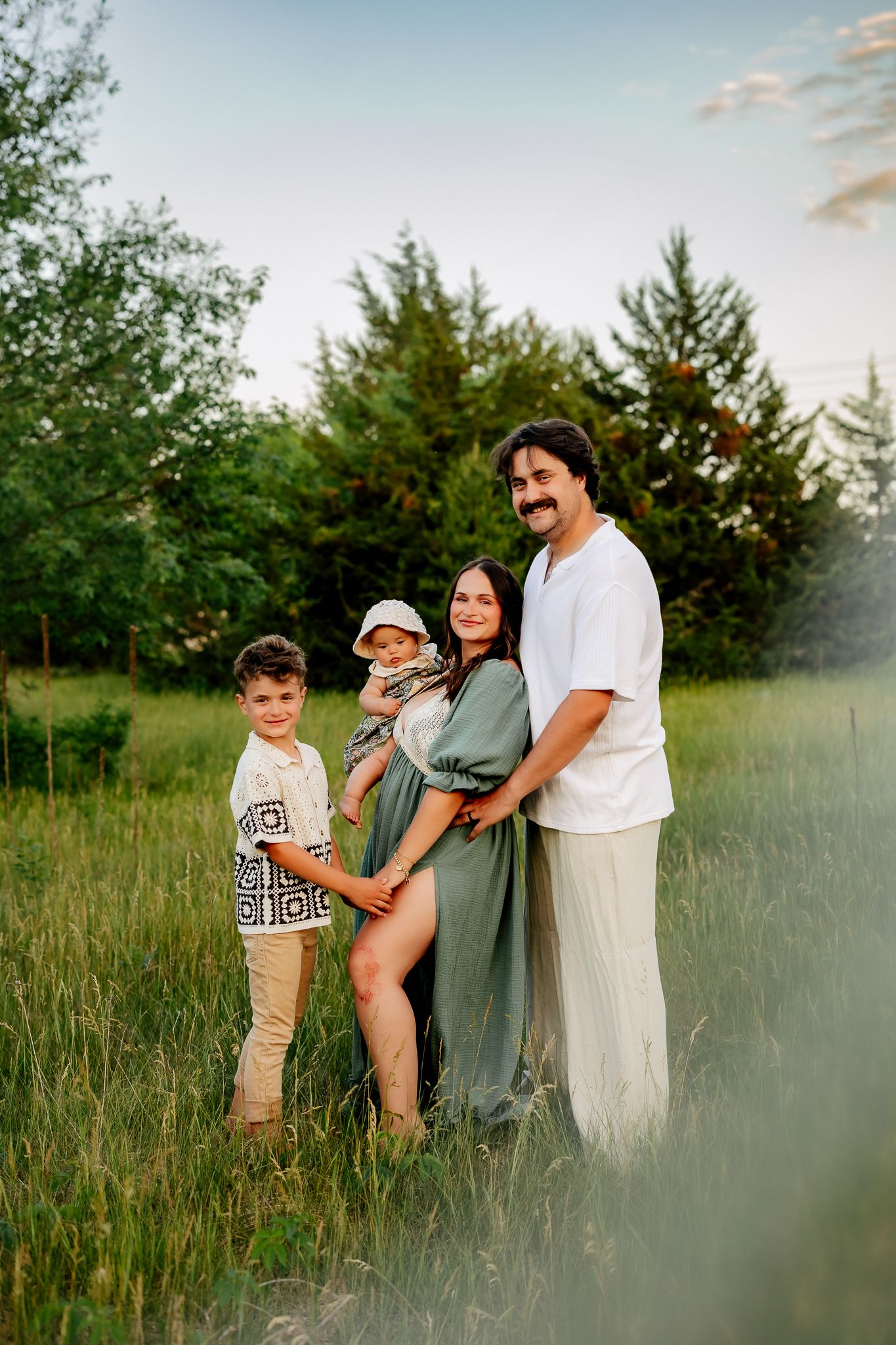 Family maternity session with pregnant mother in green dress, father and two young children outdoors.