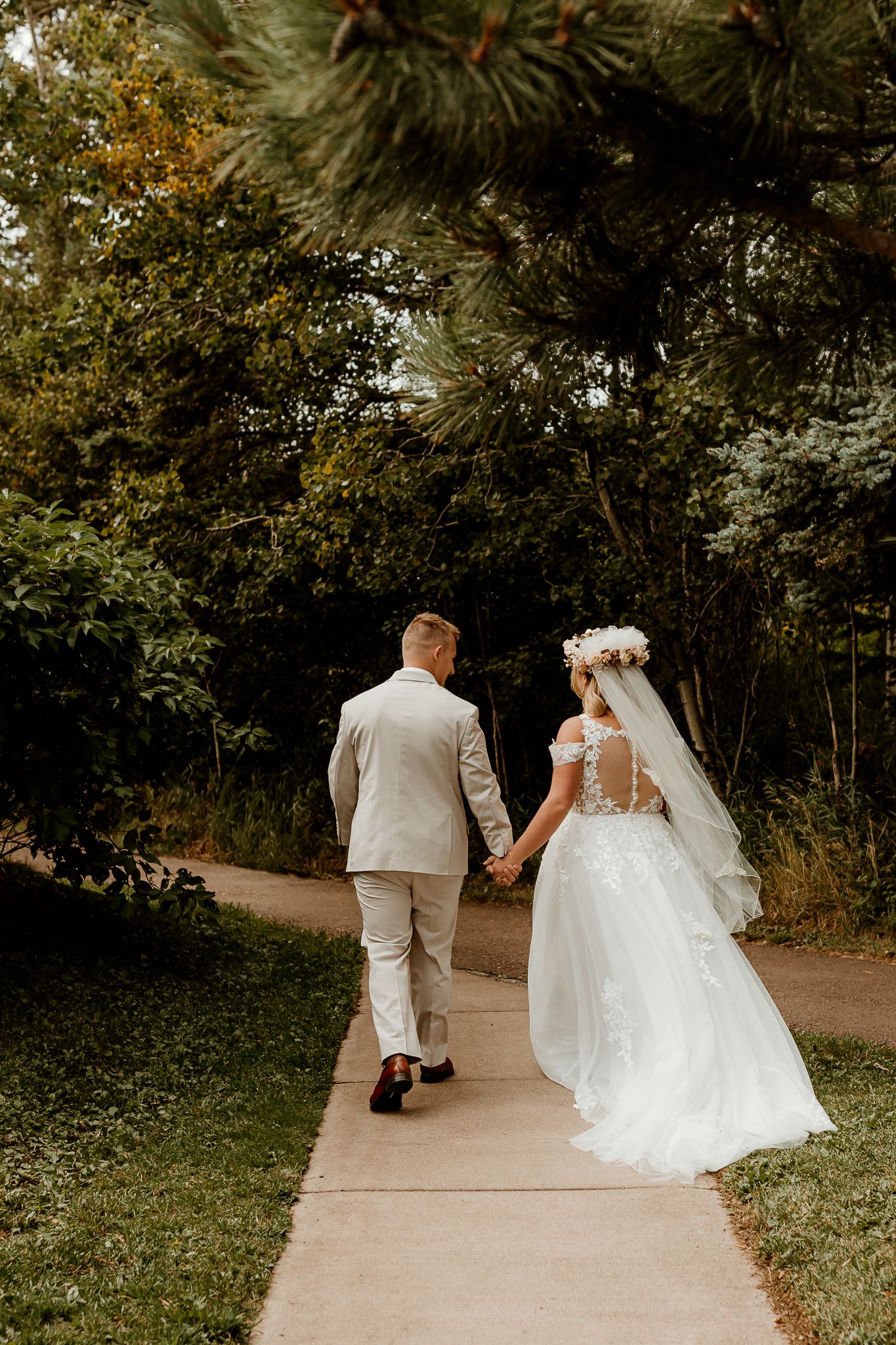 Bride and groom walking hand in hand down a garden path, bride wearing white gown with floral crown and veil.