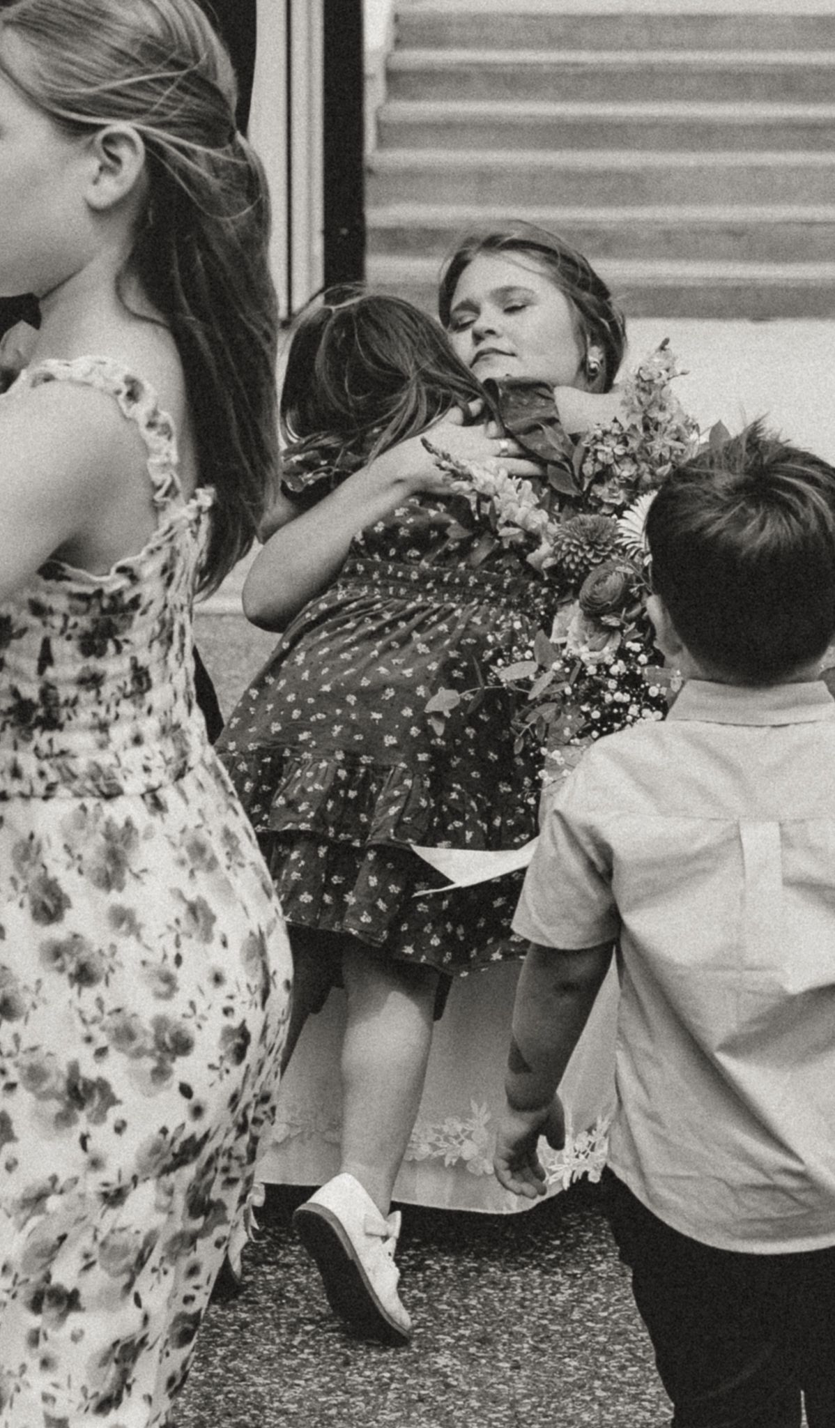 Black and white photo of children hugging and sharing flowers on steps, capturing a tender childhood moment.