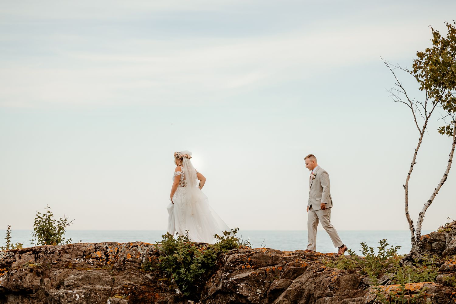 Bride and groom walk along rocky coastal cliffs with ocean views on their wedding day.