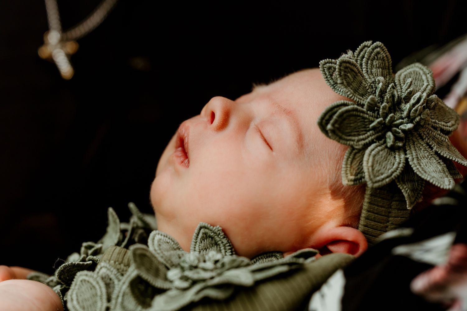 Sleeping newborn baby wearing a green floral lace headband and matching outfit, captured in a soft portrait.