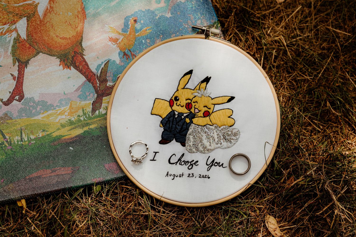 Pikachu wedding ring holder embroidery hoop with I Choose You August 22 2016 inscription and two gold rings.