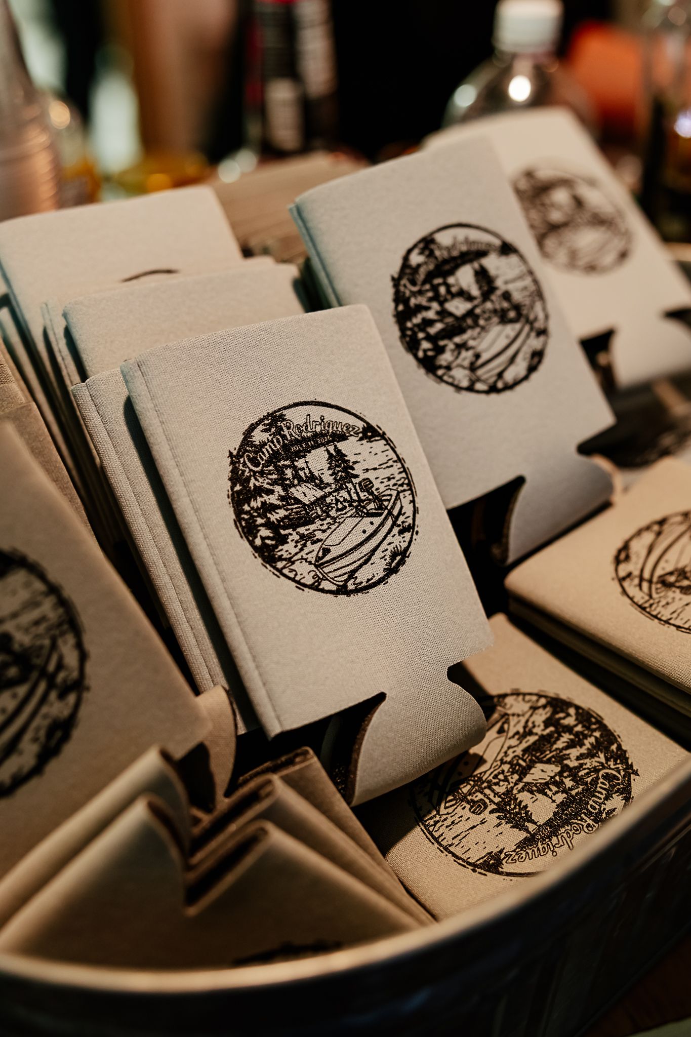 Decorative beer koozies with circular black ink designs displayed in a bowl at an event.