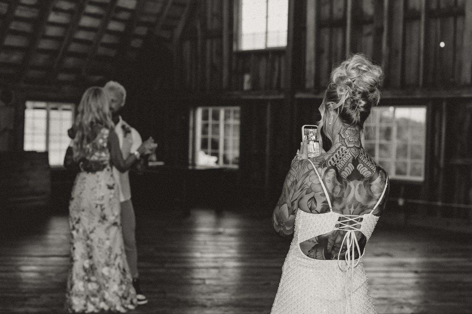 Black and white photo of two women in dresses inside a rustic barn at a wedding celebration.