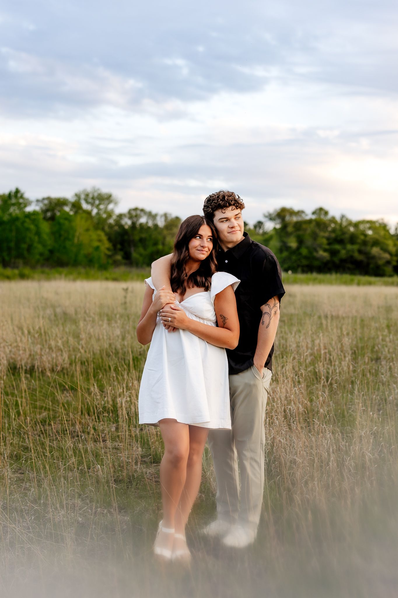 Young couple embracing in a golden field at sunset, woman in white dress, man in black shirt.