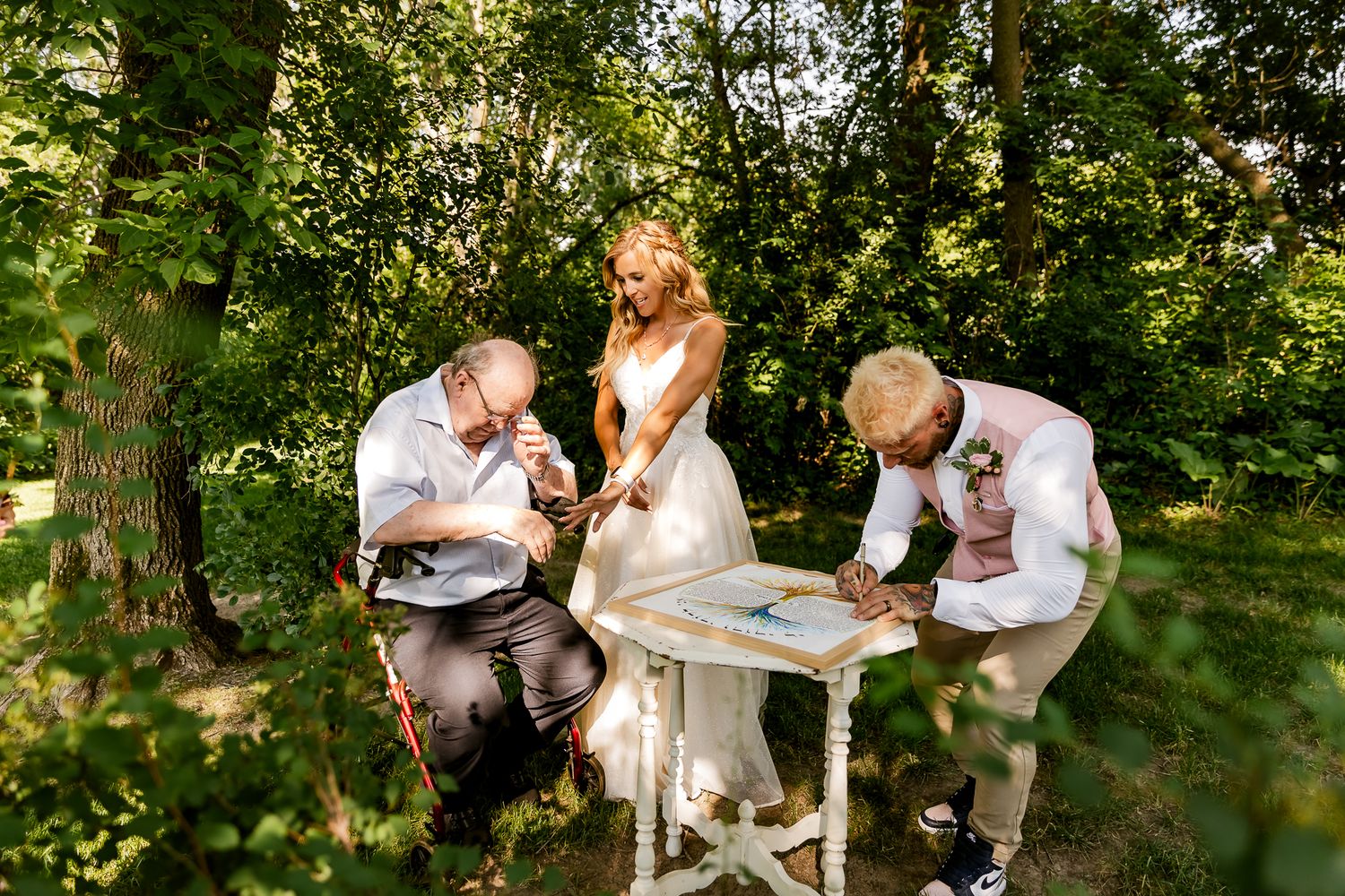 Bride and groom signing wedding documents outdoors surrounded by lush green trees during an intimate garden ceremony.