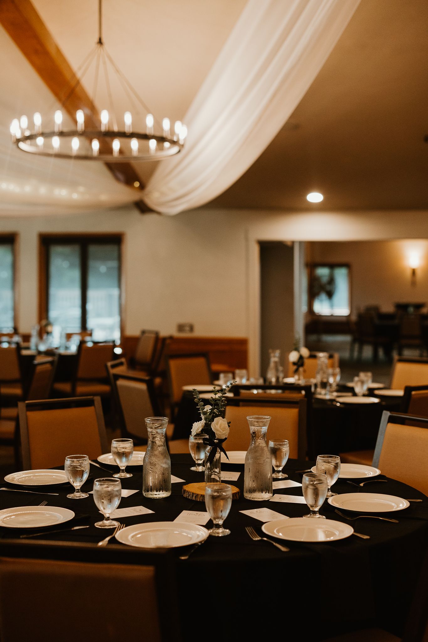 Elegant banquet hall with black tablecloths, white plates, glass stemware, floral centerpieces, and a candle chandelier.