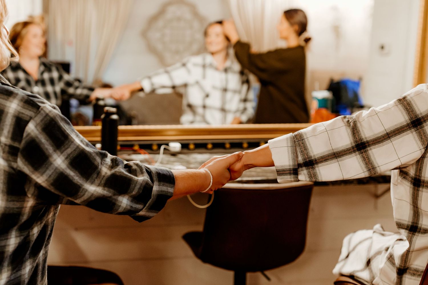 Group of people in plaid shirts holding hands in a circle inside a bright, cozy room with a wooden counter and chairs.