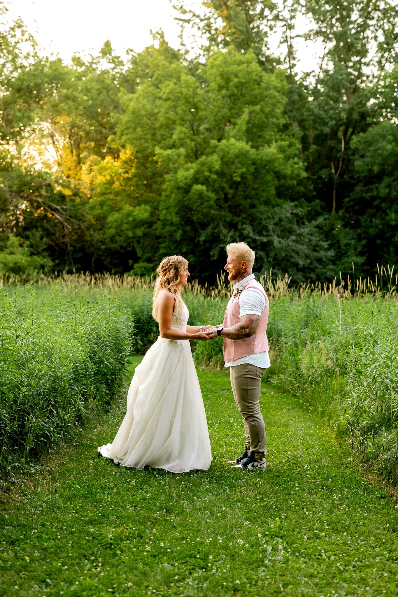Bride and groom holding hands in a lush green garden at golden hour during an outdoor wedding ceremony.
