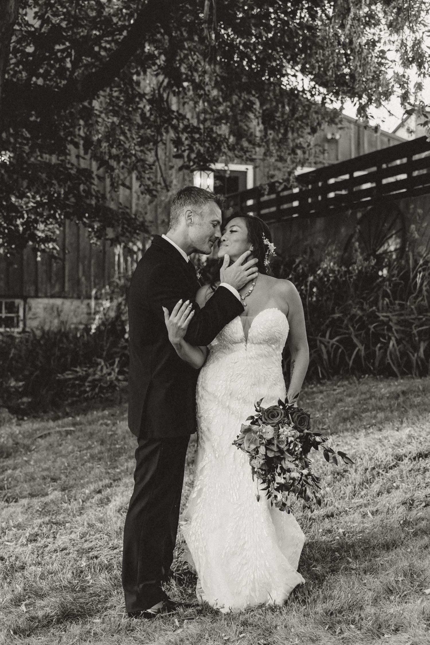Black and white photo of a bride and groom sharing a romantic kiss outdoors on their wedding day.
