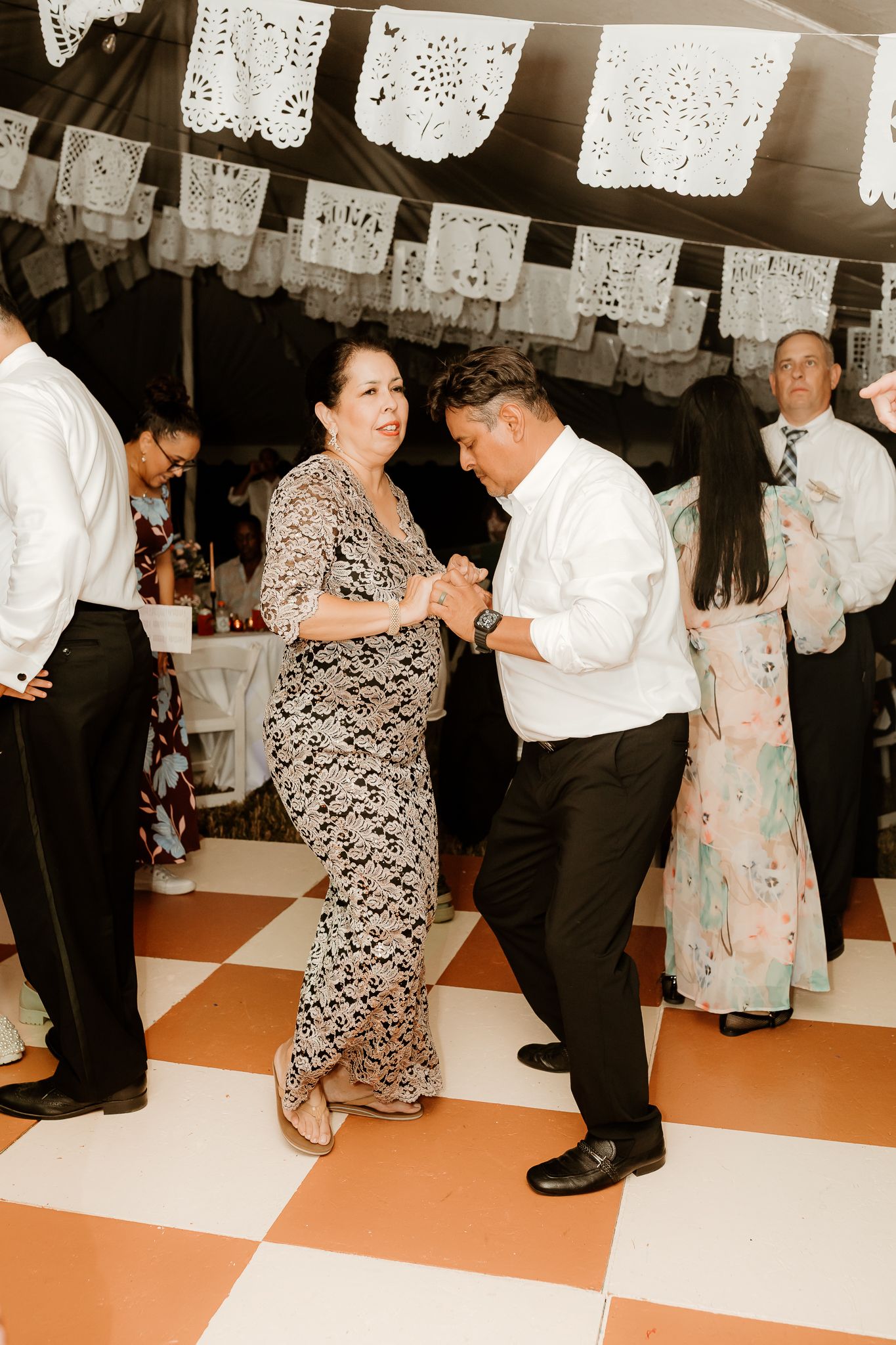 Couple dancing at a festive reception under papel picado decorations on a checkered dance floor.