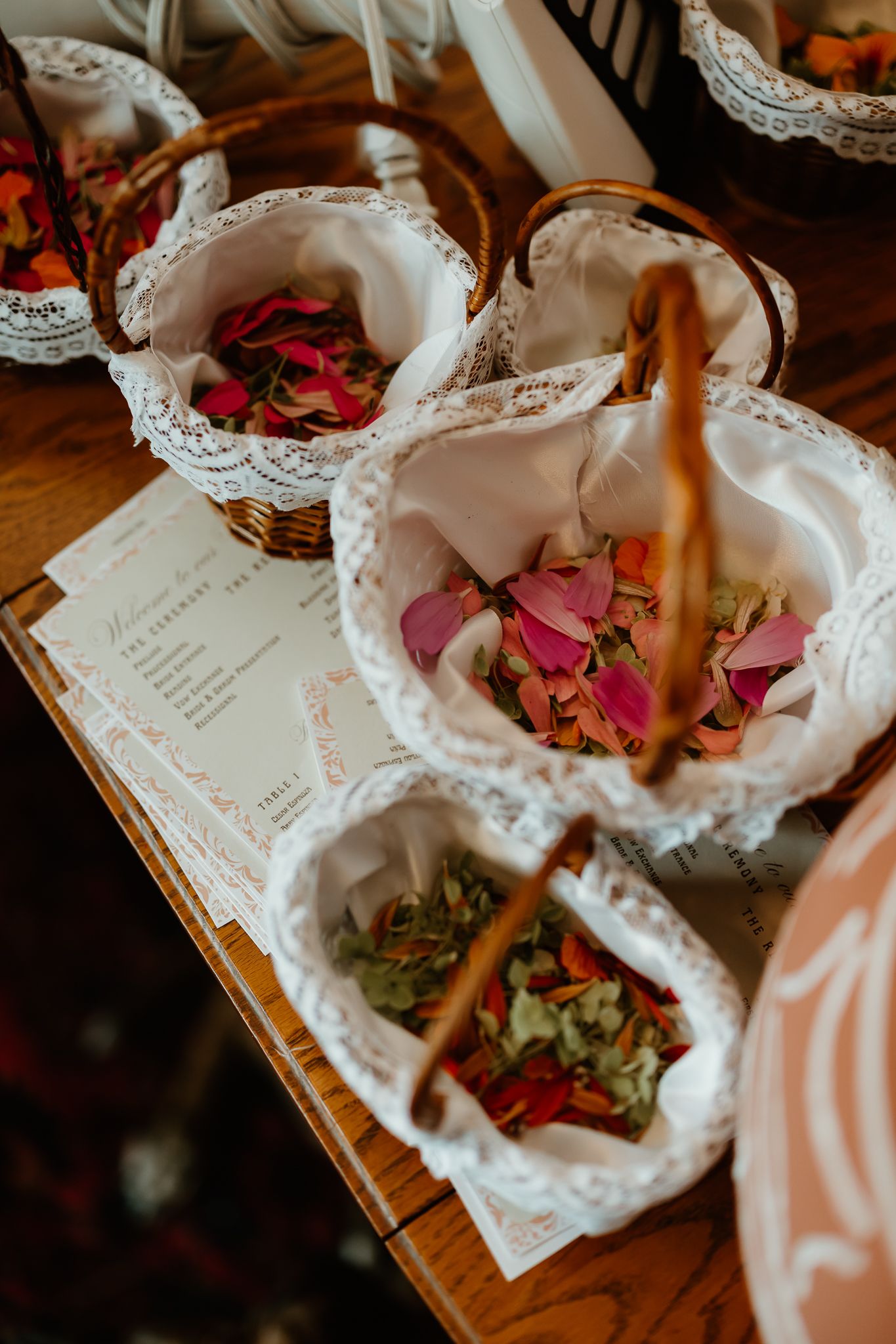 Wicker baskets lined with lace filled with colorful rose petals on a wooden table at a wedding ceremony.