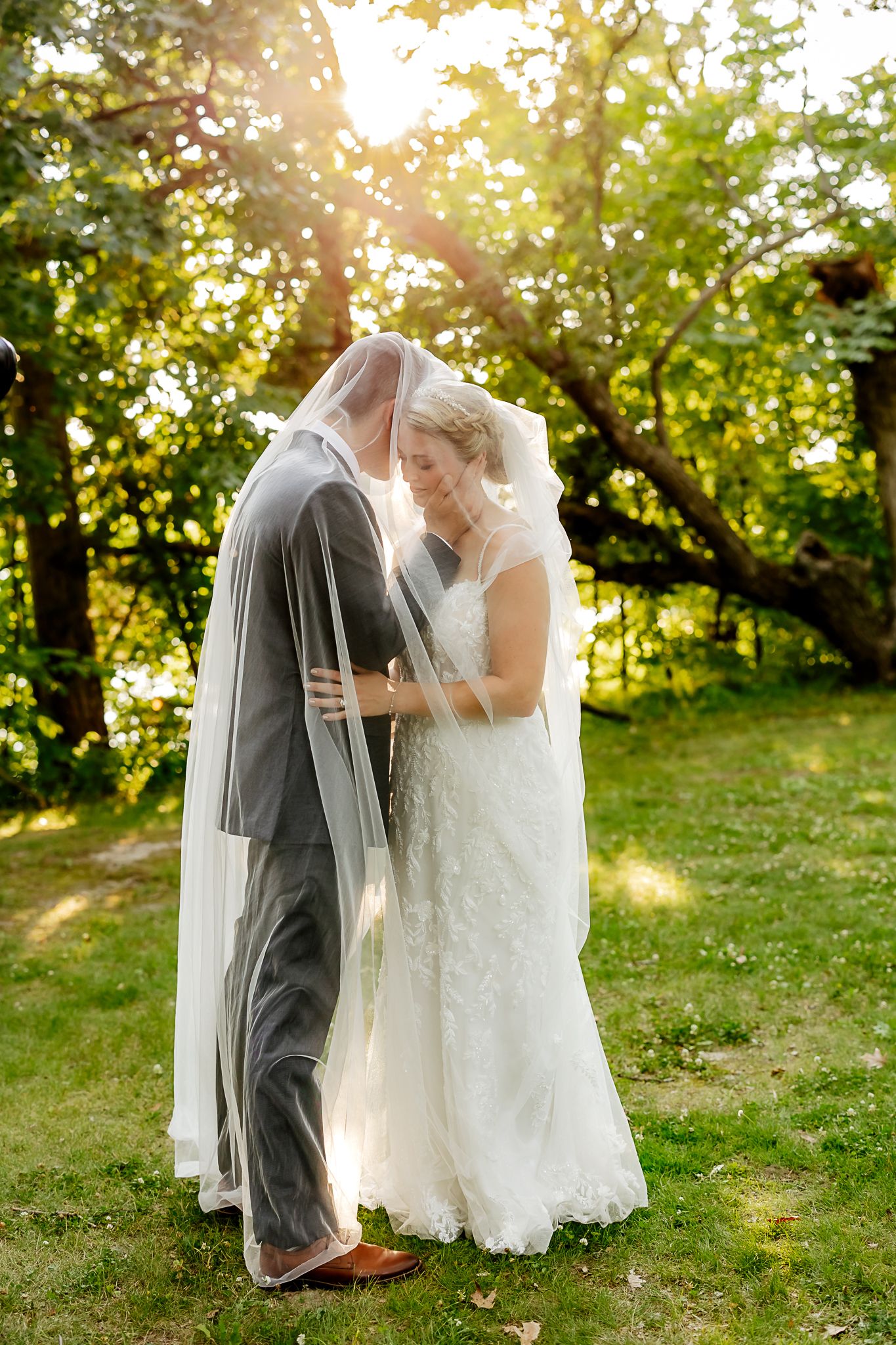 Bride and groom share romantic moment under wedding veil in sunlit garden setting.