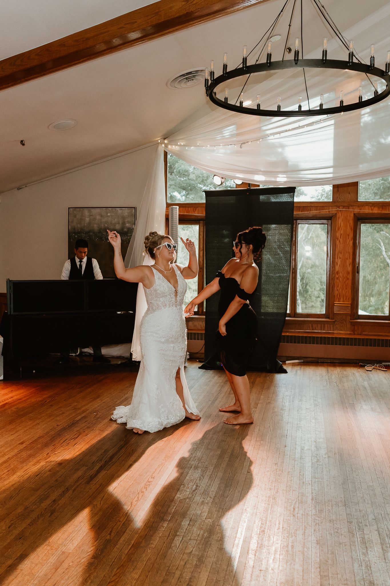 Bride in white gown dancing with guest in black dress on wooden dance floor at elegant wedding reception venue.