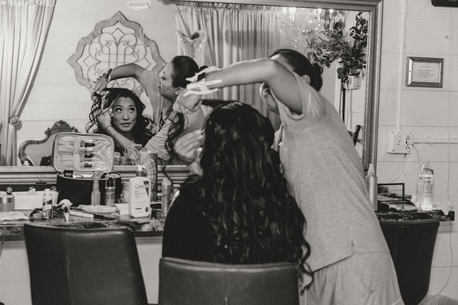 Black and white photo of a woman getting hair styled at a vanity mirror in a beauty salon.