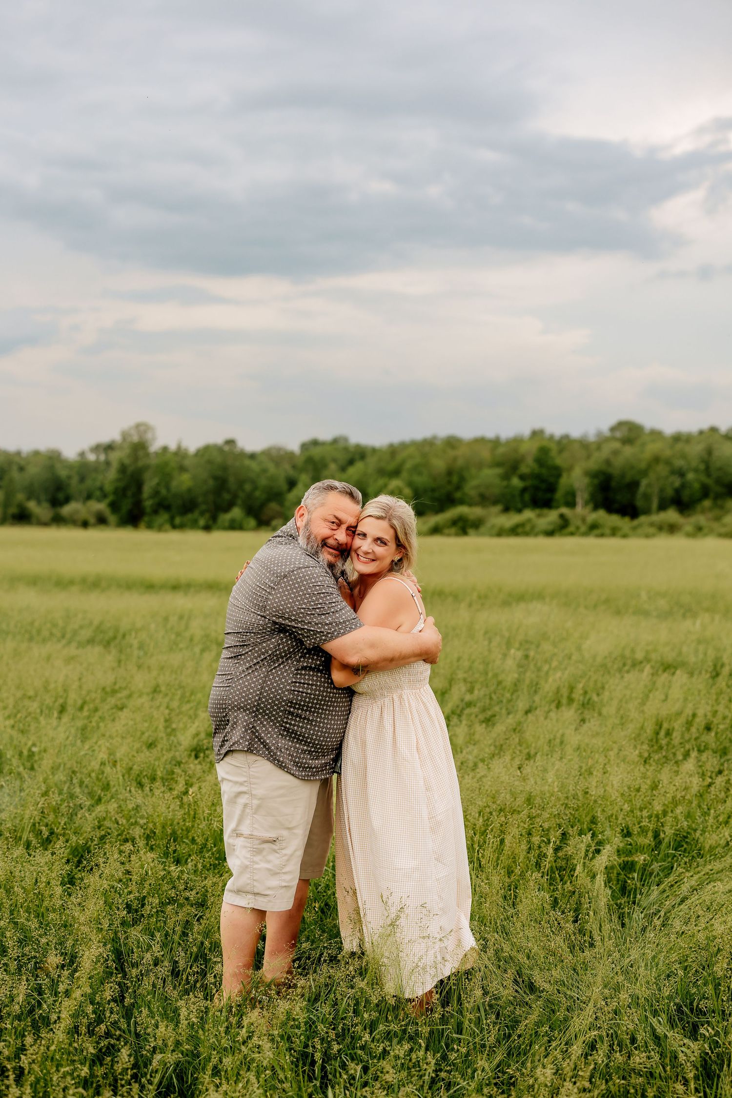 Happy couple embracing and smiling in a green meadow with cloudy skies.