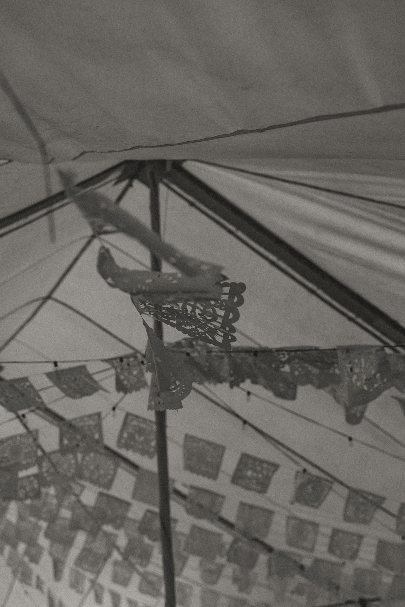 Black and white photo of papel picado decorations hanging inside a tent ceiling.