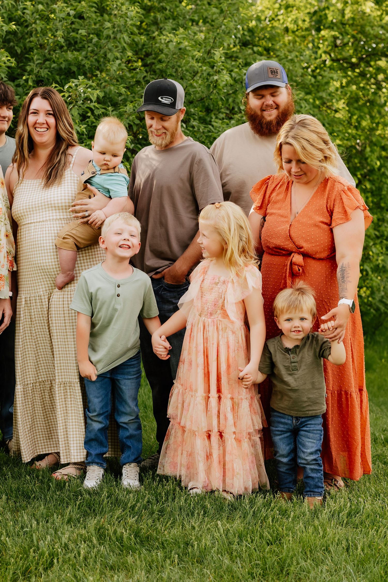 Parents with young children and toddlers smiling together outdoors in casual coordinated family portrait.
